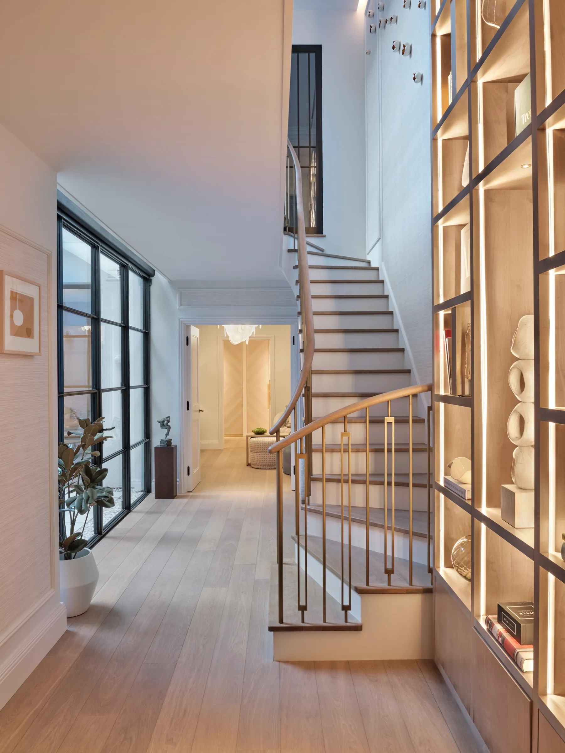 Hallway with a curved staircase and illuminated bespoke shelving
