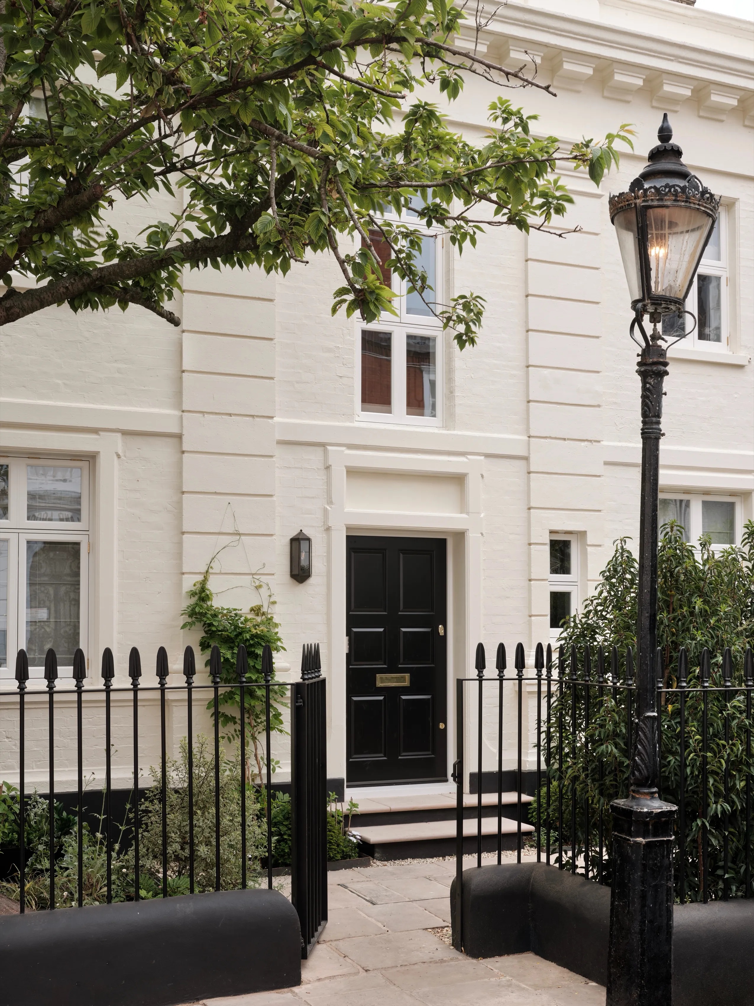 A restored white stucco townhouse with black railings and a period street lamp